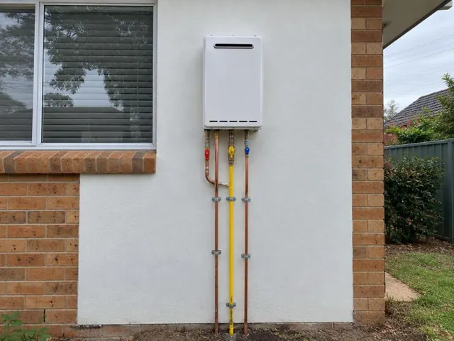 Wall-mounted hot water unit with copper and gas pipes on a brick exterior wall in Peakhurst