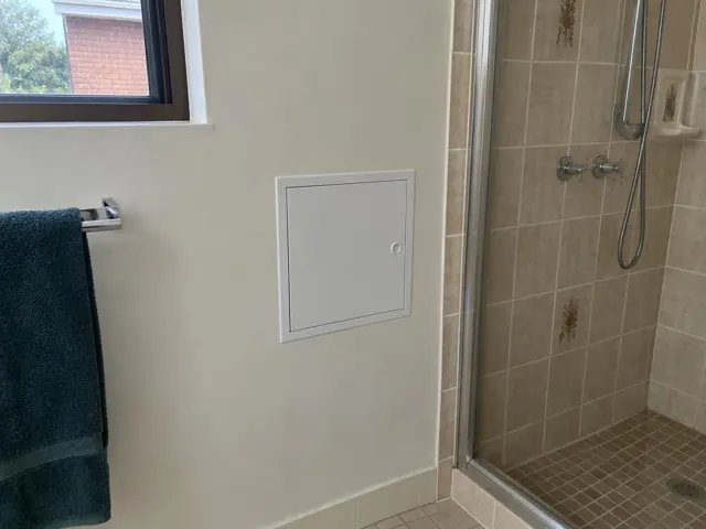Small white access panel on a bathroom wall beside a tiled shower in Riverwood